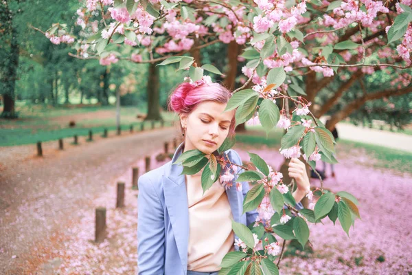 Moda mavi pantolon takım ayakta yanındaki renkli çiçekler pembe saçlı güzel kız. . Oldukça yumuşak modeli fotoğraf makinesine benziyor.