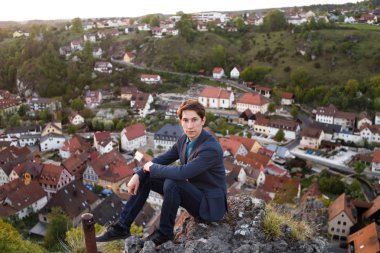 takım elbiseli bir adam gözlem güverte üzerinde oturur ve tarihi eski şehir Pottenstein Almanya yukarıda eski kasaba evleri görünümünü bakar.