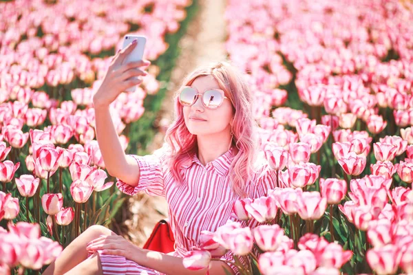 在阳光明媚的春日 年轻女子戴太阳镜在郁金香花田自拍自拍 — 图库照片