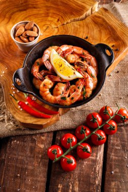 Tavada baharatlı karides, sarımsak, kişniş ve biber, sonraki yemek malzemeleri, ahşap arka planda domatesler.