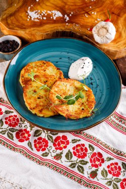 Patatesli gözlemelerin yakın plan görüntüsü. Ulusal modelin arka planında mavi bir tabakta patates keki, taze maydanozlu ve ekşi kremalı..