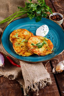 Patatesli kreplerin yakından görünümü. Taze maydanoz ve ekşi krema ile ahşap bir masa üzerinde mavi bir tabak üzerinde Patates kek. Metin için alan kopyalama.