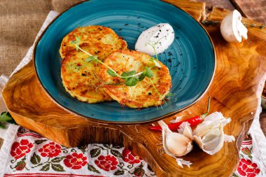 Patatesli gözlemelerin yakın plan görüntüsü. Ulusal modelin arka planında mavi bir tabakta patates keki, taze maydanozlu ve ekşi kremalı..