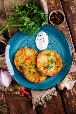 Patatesli kreplerin yakından görünümü. Taze maydanoz ve ekşi krema ile ahşap bir masa üzerinde mavi bir tabak üzerinde Patates kek. Metin için alan kopyalama.