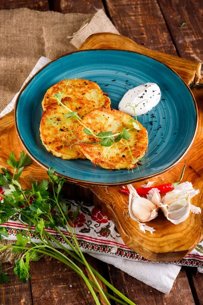 Patatesli gözlemelerin yakın plan görüntüsü. Ulusal modelin arka planında mavi bir tabakta patates keki, taze maydanozlu ve ekşi kremalı..