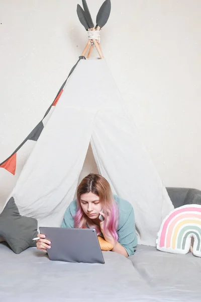 一位年轻的母亲在家里的平板电脑上工作 在一间由床单制成的儿童房里 大流行病期间的检疫概念 — 图库照片