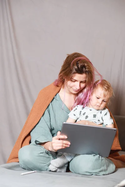 Stay at home, mom works remotely on a laptop computer, taking care of her child. A young mother on maternity leave is trying to work as a freelancer with a baby. Close up