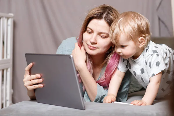 Stay at home, mom works remotely on a laptop computer, taking care of her child. A young mother on maternity leave is trying to work as a freelancer with a baby. Close up