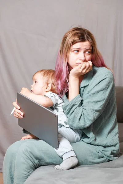 A young woman works at home with a tablet computer, along with a child.the son wants to communicate with his mother, they make noise and interfere with work.Self-isolation during the coronovirus pandemic