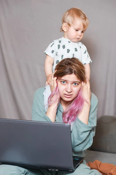 Stay at home, mom works remotely on a laptop, taking care of her child. A young mother on maternity leave is trying to work as a freelancer with a baby. Close up