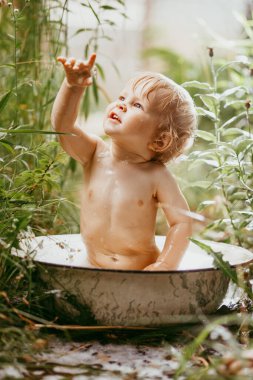 Güneşli bir yaz günü. Sevimli küçük bir çocuk yeşil bir çimenlikte banyo yapıyor. Suyla ıslanmış, su sıçrıyor ve gülüyor..