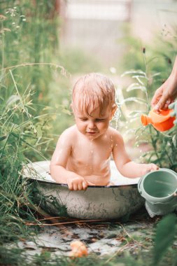Güneşli bir yaz günü. Sevimli küçük bir çocuk yeşil bir çimenlikte banyo yapıyor. Suyla ıslanmış, su sıçrıyor ve gülüyor..