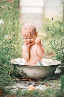 Güneşli bir günde, yeşil bir bahçede galvanizli bir banyoda banyo yapan sevimli, komik bir çocuk.