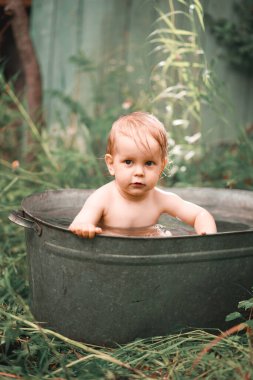 Küçük bir çocuk yazın yeşil bir bahçede havuzda yıkanır..