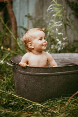 Küçük bir çocuk yazın yeşil bir bahçede havuzda yıkanır..