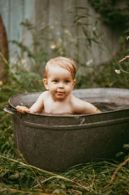 Küçük bir çocuk yazın yeşil bir bahçede havuzda yıkanır..