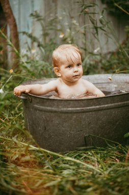 Küçük bir çocuk yazın yeşil bir bahçede havuzda yıkanır..