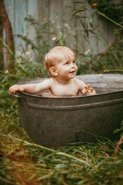 Küçük bir çocuk yazın yeşil bir bahçede havuzda yıkanır..