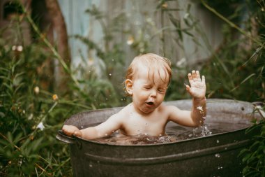 Küçük bir çocuk yazın yeşil bir bahçede havuzda yıkanır..