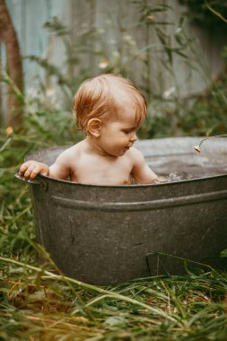 Küçük bir çocuk yazın yeşil bir bahçede havuzda yıkanır..