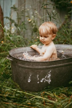 Küçük bir çocuk yazın yeşil bir bahçede havuzda banyo yapar. Yanlara su sıçratır.