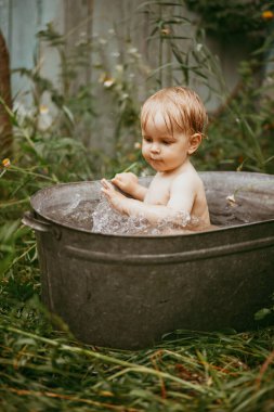 Küçük bir çocuk yazın yeşil bir bahçede havuzda banyo yapar. Yanlara su sıçratır.