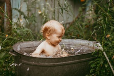 Küçük bir çocuk yazın yeşil bir bahçede havuzda banyo yapar. Yanlara su sıçratır.