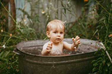 Küçük bir çocuk yazın yeşil bir bahçede havuzda banyo yapar. Yanlara su sıçratır.