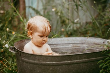 Küçük bir çocuk yazın yeşil bir bahçede havuzda banyo yapar. Yanlara su sıçratır.
