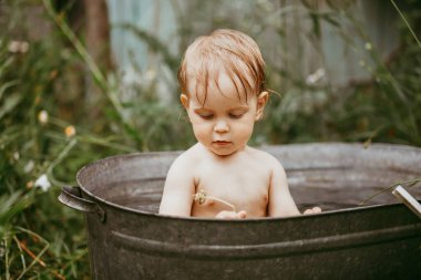 Güneşli bir günde, yeşil bir bahçede galvanizli bir banyoda banyo yapan sevimli, komik bir çocuk.