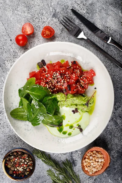 Exquisite fish tartare raw tuna fillet with greens close up on a white plate