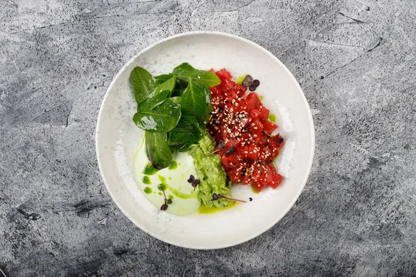 Exquisite fish tartare raw tuna fillet with greens close up on a white plate