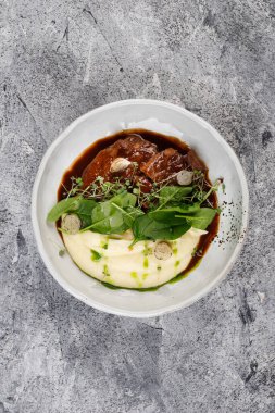 Patates ve lahana soslu dana yanakları, beyaz bir tabakta otlarla süslenmiş.