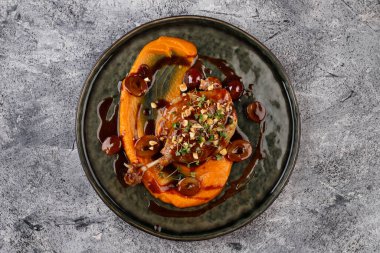 Soslu, üzümlü, otlu ve fındıklı kızarmış ördek budu ve bembeyaz bir tabak. Restoranda menü var.