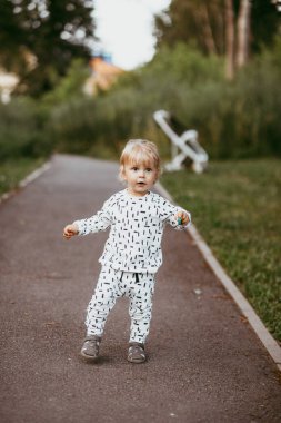 Doğanın arka planına karşı güzel beyaz bir takım elbiseyle yürüyen tatlı bir çocuk. Bir yaşında bir çocuk öğreniyor ve dışarıda oynuyor..
