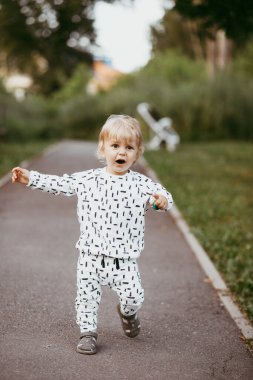Doğanın arka planına karşı güzel beyaz bir takım elbiseyle yürüyen tatlı bir çocuk. Bir yaşında bir çocuk öğreniyor ve dışarıda oynuyor..