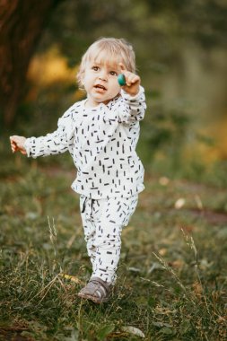 Doğanın arka planına karşı güzel beyaz bir takım elbiseyle yürüyen tatlı bir çocuk. Bir yaşında bir çocuk öğreniyor ve dışarıda oynuyor..