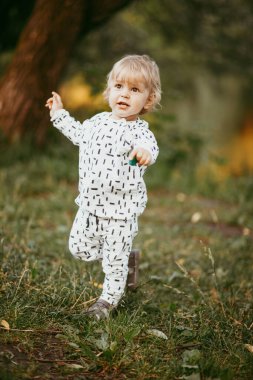 Doğanın arka planına karşı güzel beyaz bir takım elbiseyle yürüyen tatlı bir çocuk. Bir yaşında bir çocuk öğreniyor ve dışarıda oynuyor..