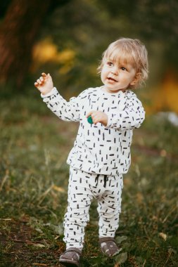 Doğanın arka planına karşı güzel beyaz bir takım elbiseyle yürüyen tatlı bir çocuk. Bir yaşında bir çocuk öğreniyor ve dışarıda oynuyor..
