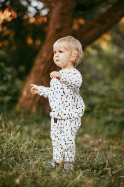 Doğanın arka planına karşı güzel beyaz bir takım elbiseyle yürüyen tatlı bir çocuk. Bir yaşında bir çocuk öğreniyor ve dışarıda oynuyor..