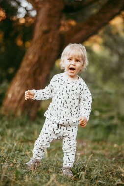 Doğanın arka planına karşı güzel beyaz bir takım elbiseyle yürüyen tatlı bir çocuk. Bir yaşında bir çocuk öğreniyor ve dışarıda oynuyor..