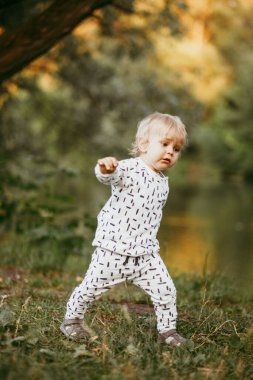 Doğanın arka planına karşı güzel beyaz bir takım elbiseyle yürüyen tatlı bir çocuk. Bir yaşında bir çocuk öğreniyor ve dışarıda oynuyor..