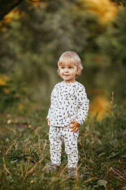 Doğanın arka planına karşı güzel beyaz bir takım elbiseyle yürüyen tatlı bir çocuk. Bir yaşında bir çocuk öğreniyor ve dışarıda oynuyor..