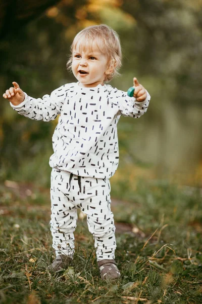 Doğanın arka planına karşı güzel beyaz bir takım elbiseyle yürüyen tatlı bir çocuk. Bir yaşında bir çocuk öğreniyor ve dışarıda oynuyor..