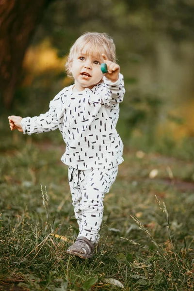 Doğanın arka planına karşı güzel beyaz bir takım elbiseyle yürüyen tatlı bir çocuk. Bir yaşında bir çocuk öğreniyor ve dışarıda oynuyor..