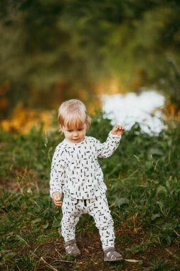 Doğanın arka planına karşı güzel beyaz bir takım elbiseyle yürüyen tatlı bir çocuk. Bir yaşında bir çocuk öğreniyor ve dışarıda oynuyor..