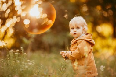 Bir sonbahar günü, gün batımında bej ceketle yürüyen tatlı bir erkek bebek.