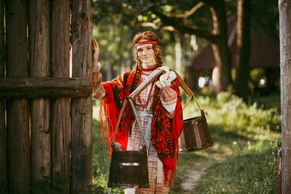 Beautiful Slavic girl with long blonde hair and brown eyes in a white and red embroidered suit and a yoke on her shoulders.Traditional clothing of the Ukrainian region.summer day