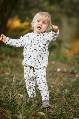 Doğanın arka planına karşı güzel beyaz bir takım elbiseyle yürüyen tatlı bir çocuk. Bir yaşında bir çocuk öğreniyor ve dışarıda oynuyor..