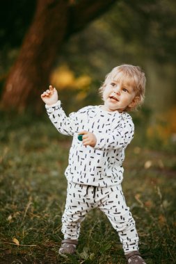 Doğanın arka planına karşı güzel beyaz bir takım elbiseyle yürüyen tatlı bir çocuk. Bir yaşında bir çocuk öğreniyor ve dışarıda oynuyor..